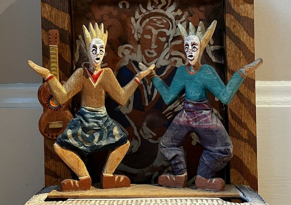 Colorful and fun Diorama with tiny figures wearing masks on a stage with carvings and a backdrop of dynamic paintings