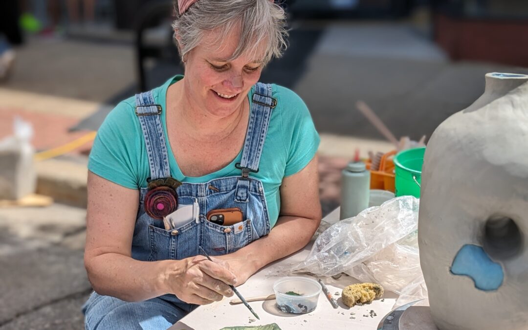 Pottery teacher demonstrating coil building an interesting tall vase with an opening in the side, textural pieces painted blue to decorate the side.