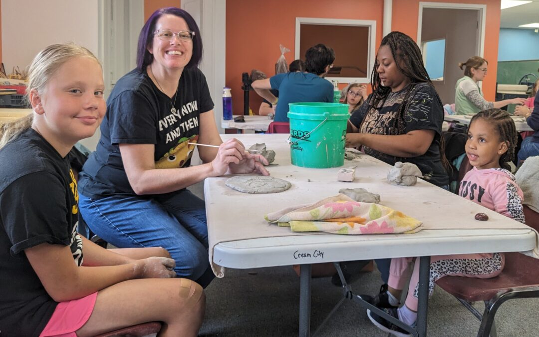 Parents and Children working on wet clay projects at a table. Children are various ages