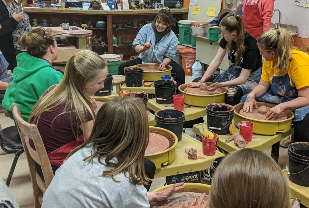 Pottery wheels with seated students listening to their instructor