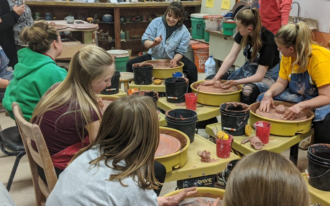 Pottery wheels with seated students listening to their instructor